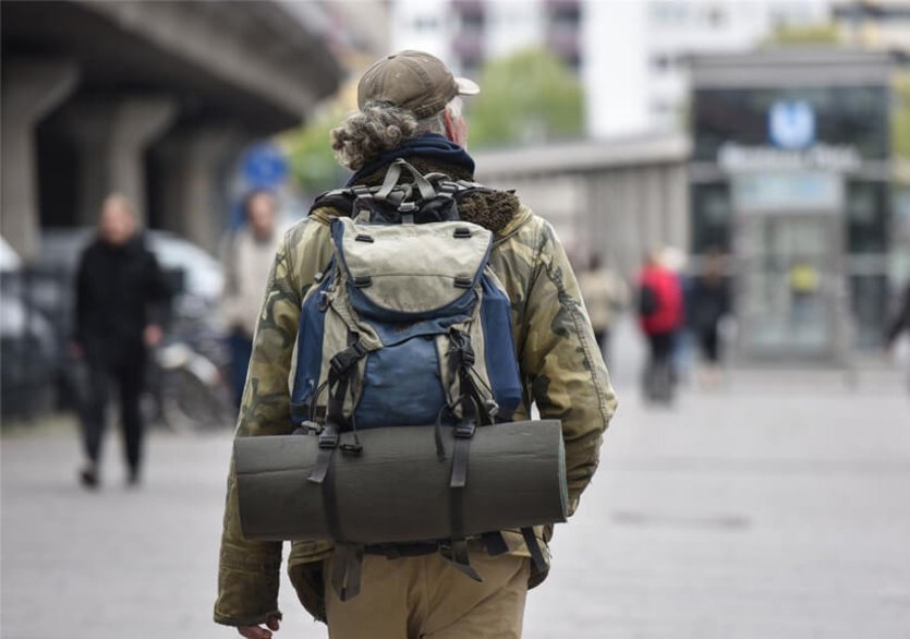 Ein obdachloser Mann mit Rucksack von hinten läuft durch die Stadt