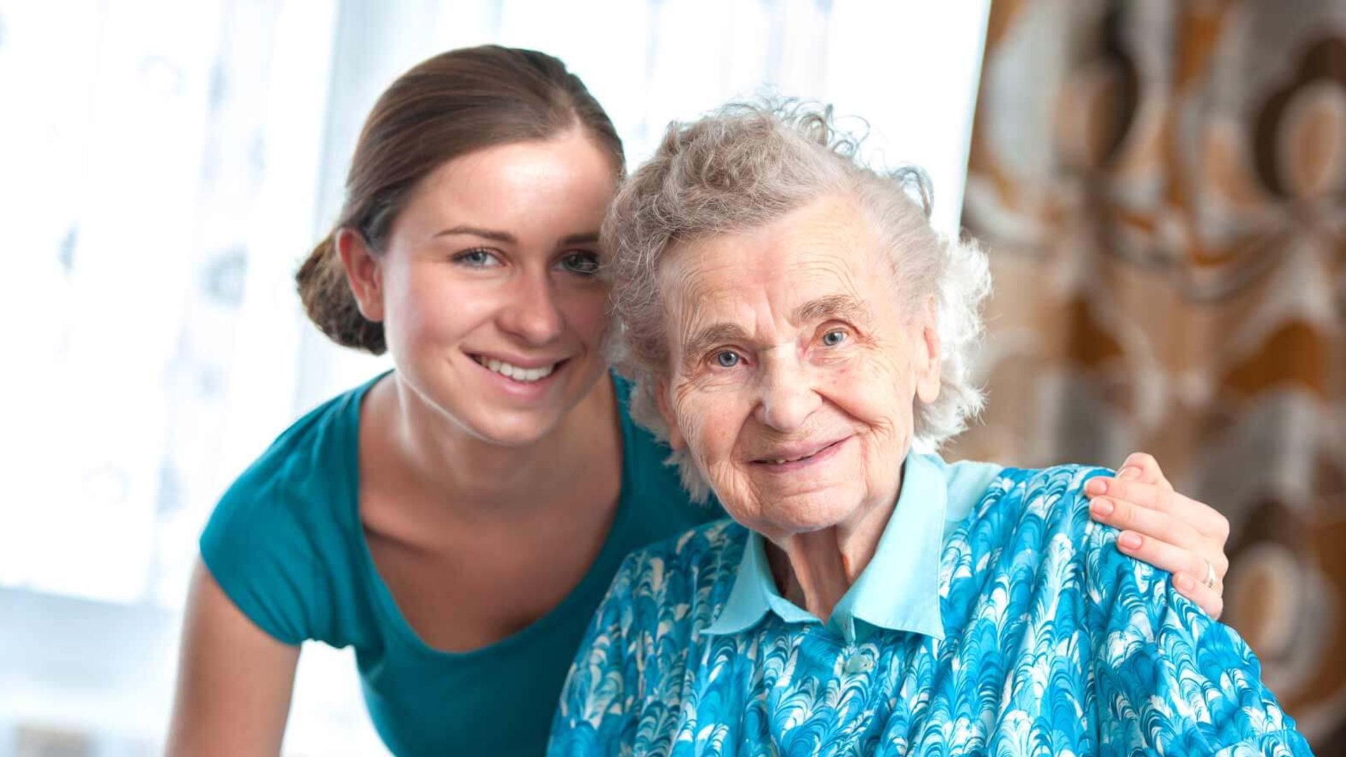 Lächelnde Pflegerin mit Seniorin im Arm